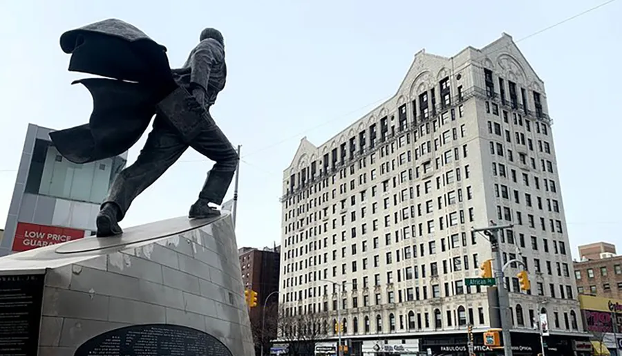 The image shows a statue of a person carrying a large curved object, set against the backdrop of an ornate building and a cloudy sky.