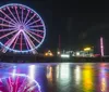 A colorful boat labeled Atlantic City sits on the shore with a large Ferris wheel and an amusement park on a pier in the background