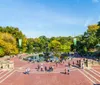 This image shows a bustling Bethesda Terrace overlooking the Bethesda Fountain in Central Park New York City with people enjoying a sunny day amidst the changing colors of autumn leaves