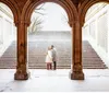 A couple shares an affectionate moment under an ornate arched passageway with a staircase in the background