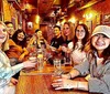A group of people is happily socializing around a long table inside a cozy bar or restaurant with drinks in front of them