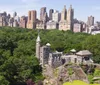 An aerial view of Belvedere Castle amidst the lush greenery of Central Park with the Manhattan skyline in the background