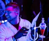 Two people wearing lab coats and safety glasses are working with glowing green chemicals in a laboratory setting