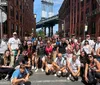A diverse group of people pose for a photo on a sunny day with the iconic Manhattan Bridge in the background