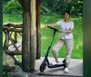 Two people wearing helmets are enjoying a ride on electric scooters near a historical archway in a park setting