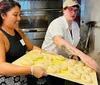 Three smiling people are holding up large seeded bagels toward the camera in a kitchen setting