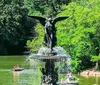 A person is standing in front of a serene pond with towering buildings in the background likely in a city park