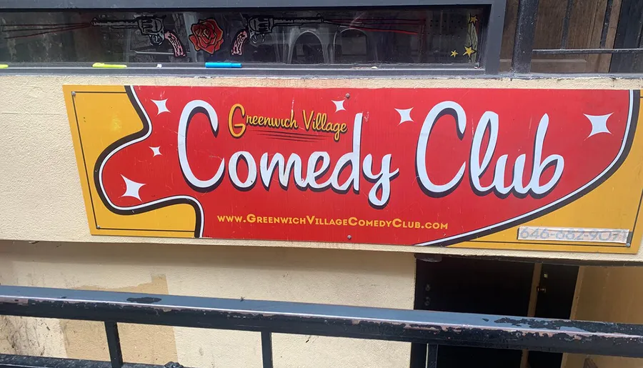 The image shows a vibrant sign for the Greenwich Village Comedy Club with contact information and a web address.