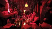 A lively bar scene with patrons enjoying drinks under the dim, warm glow of string lights and neon.