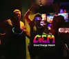 A group of people appear to be enjoying a social event at night wearing glowing headbands and accessories with a logo and text GEM - Good Energy Match superimposed onto the image