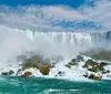 The image shows the powerful and picturesque Niagara Falls with cascades of water plunging over a crest lined with white frothy water and mist backed by a clear blue sky speckled with clouds