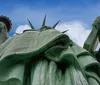 A ferry filled with passengers sails near the Statue of Liberty on a cloudy day