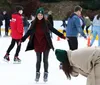 A group of people are enjoying ice skating with a smiling woman in the center balancing herself while another person appears to be bending down or falling in the foreground