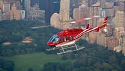 A red and white helicopter is flying over Central Park amidst the urban backdrop of a densely built cityscape.