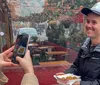 A person takes a photo of another person who is smiling and holding a tray of street food at an outdoor dining area