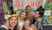 Five people are posing for a selfie with smiles in front of a store called 
