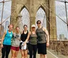 A group of five people are posing for a photo on the Brooklyn Bridge with the New York City skyline in the background