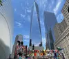 The image showcases a vibrant urban scene with the iconic One World Trade Center towering in the background adjacent to distinctive architecture and a colorful mural under a clear blue sky