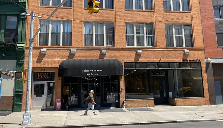 The image shows a sunny street view with a person walking by storefronts including a shop named john varvatos.