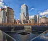 This image shows one of the two reflecting pools of the National September 11 Memorial surrounded by skyscrapers under a partly cloudy sky