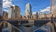 This image shows one of the two reflecting pools of the National September 11 Memorial, surrounded by skyscrapers under a partly cloudy sky.