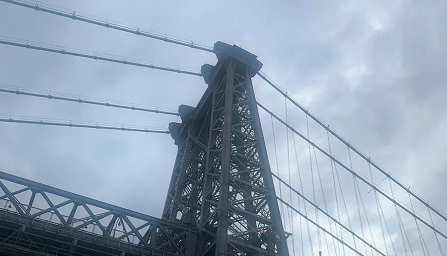 The image shows a towering bridge structure with intricate steelwork against a cloudy sky.