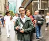 A man stands still holding a camera while the busy city life blurs around him