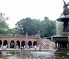 A group of people is gathered around a tour guide holding a blue umbrella in a park-like setting