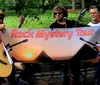 Three musicians are holding a banner that reads Rock Mystery Tour with two of them holding guitars