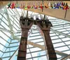 The image shows two preserved columns from a damaged structure displayed in a modern space with a glass ceiling beneath which hangs a row of colorful firefighter helmets