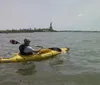 The image shows the view from a kayak on the water near the Statue of Liberty with the New York City skyline in the background