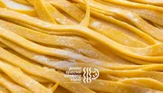 The image shows fresh, uncooked fettuccine pasta with a dusting of flour, along with text suggesting it is related to a special pasta cooking class.