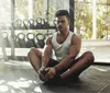 A person is stretching on the floor of a gym with weights in the background bathed in natural light coming through large windows