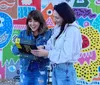 Three smiling individuals are taking a selfie on a sunny day on a city street holding a black binder or folder with a bright yellow label