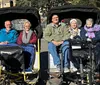 The image shows four smiling adults seated in two pedal-powered rickshaws enjoying a sunny day outdoors