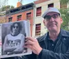 A person is holding an image of the iconic facade of the CBGB music club in front of the current John Varvatos store which now occupies the same location