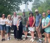 A group of people is posing joyfully with raised arms in front of a fountain in a park on a sunny day