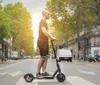 An electric scooter stands abandoned by an ornate metal fence with a scenic view of a city skyline across a body of water