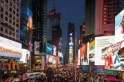 The image shows the vibrant Times Square in New York City at dusk, bustling with people and illuminated by numerous bright digital billboards.