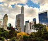 The image shows a view of a park in an urban setting with the Empire State Building towering in the background amidst other high-rise buildings under a clear blue sky