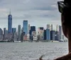 A persons silhouette in the foreground looks towards a cloudy Manhattan skyline featuring the One World Trade Center