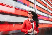 A stylish woman in a red jacket and sunglasses walks confidently in front of a vibrant red LED display.