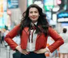 A stylish woman in a red jacket and sunglasses walks confidently in front of a vibrant red LED display