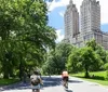 Cyclists and pedestrians enjoy a sunny day on a tree-lined path with an imposing building in the background