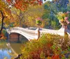 The image shows a statue of an angel with outstretched wings atop a fountain framed by an archway with a backdrop of autumnal trees