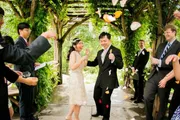 A joyful couple walks through an archway as guests throw flower petals to celebrate their wedding.