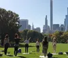 A group of people are posing joyfully on yoga mats in a sunny park with autumn foliage in the background