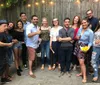 A group of smiling people are posing for a photo at an outdoor gathering some holding drinks and snacks suggesting a social event or celebration