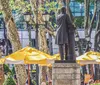 A group of people is standing around the Fearless Girl statue each adopting a similar pose with their hands on their hips emulating the statues confident stance