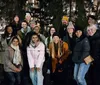 A group of smiling people pose for a photo at an outdoor evening gathering wearing winter clothing